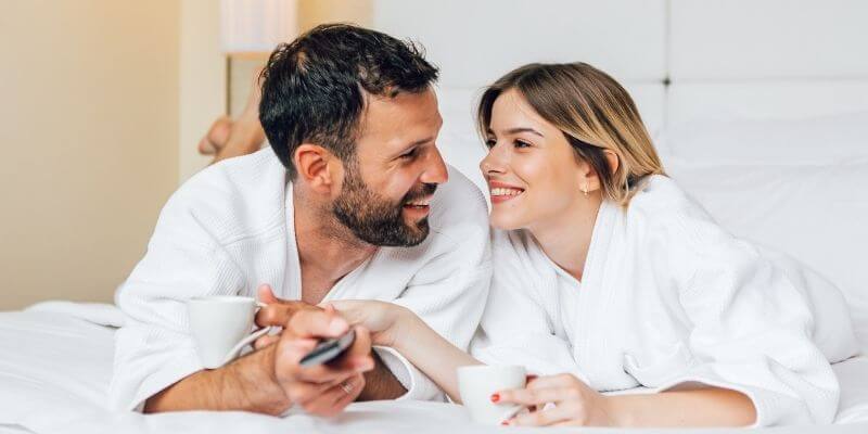 How to be more romantic a couple wrapped in robes laying on the bed